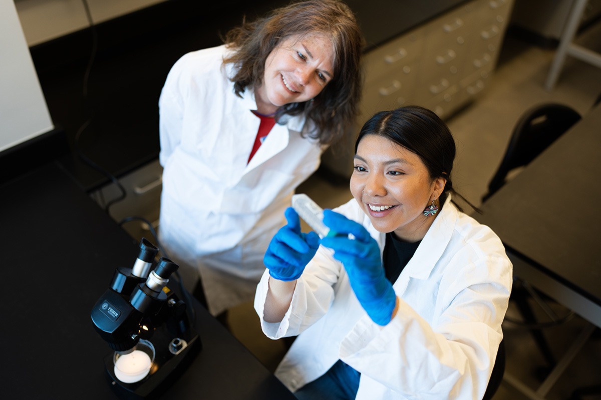 A faculty member working with a student looking at a vial in full PPE.